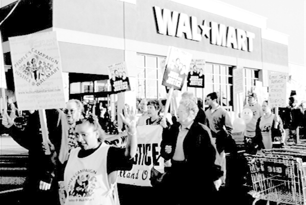 Ein Schwarz-Weiß-Bild von Menschen, die protestieren und Plakate halten, vor einem Einkaufszentrum.