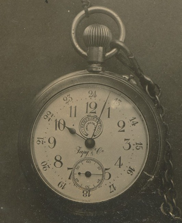 Ein Schwarz-Weiß-Foto einer alten Taschenuhr mit einer Kette, das eine nummerierte Ziffernblätter zeigt.
