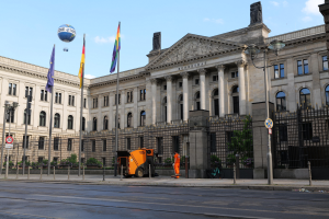 Großes modernes Gebäude mit zahlreichen Fenstern, als Bundestag in Berlin, Deutschland identifiziert, umgeben von Straßeninfrastruktur und Fußgängern unter einem bewölkten Himmel.