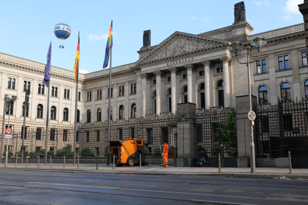 Großes modernes Gebäude mit zahlreichen Fenstern, als Bundestag in Berlin, Deutschland identifiziert, umgeben von Straßeninfrastruktur und Fußgängern unter einem bewölkten Himmel.