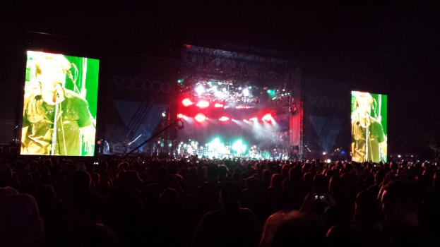 Eine Konzertszene mit einer Menge unten, einem Bildschirm links und einem weiteren Bildschirm rechts.