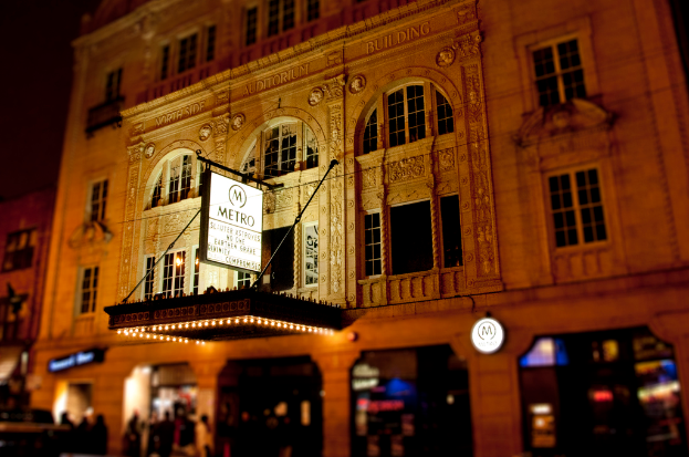 Ein gelbes Gebäude mit Geschäften im Erdgeschoss, eines davon hat eine weiße Tafel mit der Aufschrift 'Metro'.