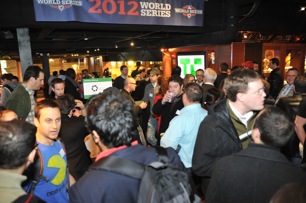 Eine große Menschenmenge bei einem Event mit einem Bildschirm, der ein Bild anzeigt, Lichtern und einer Holzwand im Hintergrund.