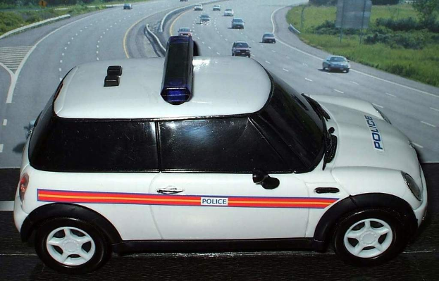 Weißer Polizeiwagen mit "Polizei"-Aufschrift auf einer Straße außerhalb der Stadt, umgeben von fließendem Verkehr, Gras und Bäumen auf beiden Seiten.