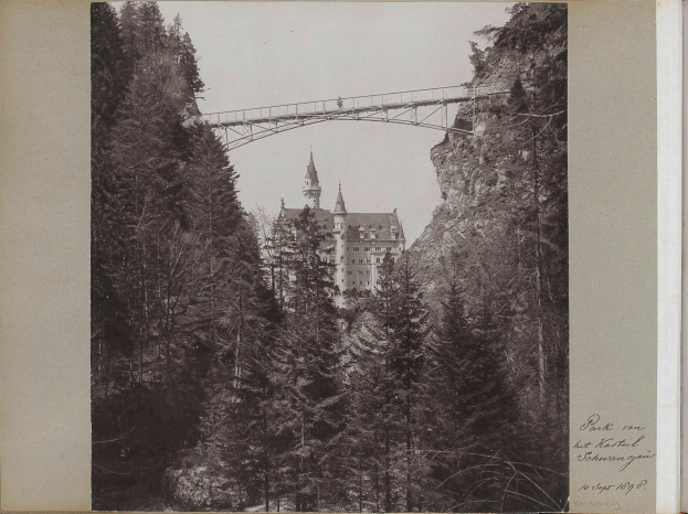 Ein Schwarz-Weiß-Foto von Schloss Neuschwanstein in Deutschland, mit einer Brücke im Vordergrund, Bäumen drumherum und Text auf der rechten Seite.