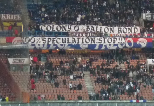 Eine Stadionansicht mit einer großen Menschenmenge, Bannern und Stühlen im Vordergrund, einem Zaun unten und einer Treppe auf der linken Seite.