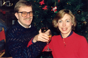 Ein Paar lächelt mit Weingläsern in der Hand vor einem Weihnachtsbaum