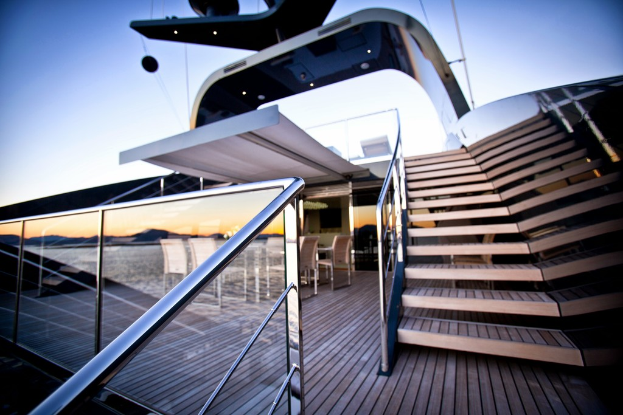 Ein modernes Glasgebäude mit Treppen auf der rechten Seite, Stühle um einen Tisch auf der linken Seite und eine Glasabsperrung unten links.