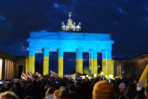 Eine Menschenmenge steht vor dem Brandenburger Tor in Berlin, Deutschland, mit Fahnen und Plakaten in den Händen, mit einer Banner auf der rechten Seite.