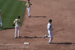 Ein Mann in einem weißen Kleid und schwarzer Mütze läuft rechts, während zwei Personen in gelben T-Shirts in der Mitte laufen, wahrscheinlich beim Cricket.