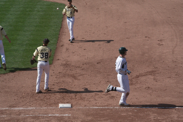 Ein Mann in einem weißen Kleid und schwarzer Mütze läuft rechts, während zwei Personen in gelben T-Shirts in der Mitte laufen, wahrscheinlich beim Cricket.