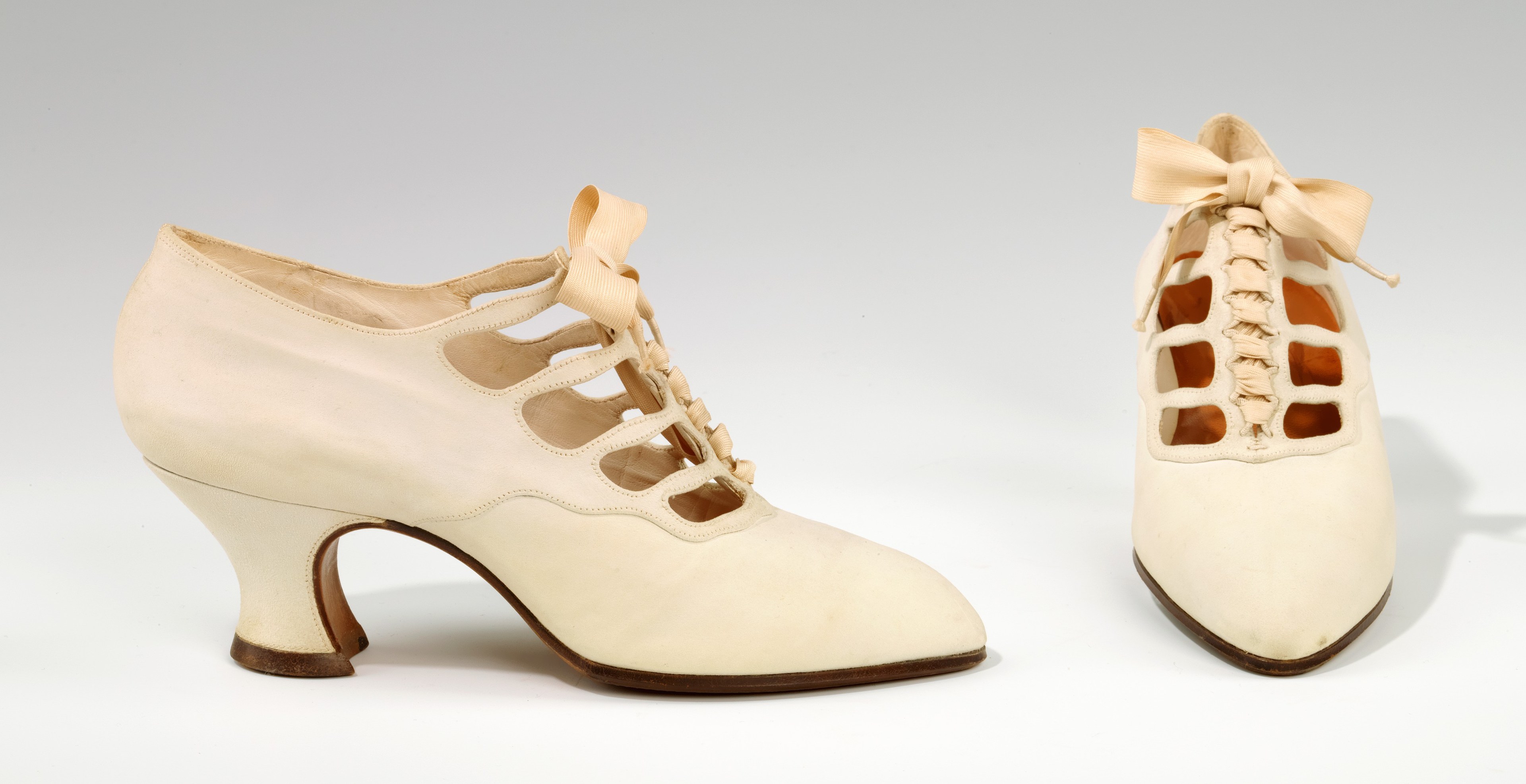 Weiße, spitz zulaufende, niedrige Pumps mit Schleife auf weißem Hintergrund.