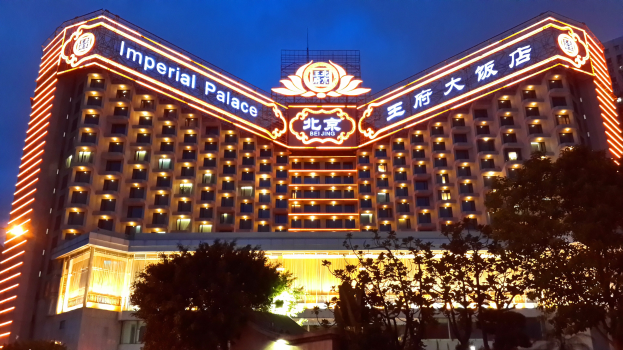 Das Hotel Imperial in Beijing, China, ein großes Gebäude mit zahlreichen Fenstern und Lichtern, das einen Namenstisch, Bäume im Vordergrund und einen klaren blauen Himmel im Hintergrund zeigt.