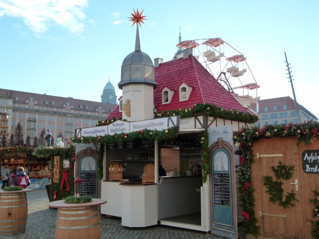 Kleines Gebäude mit rotem Dach und einem Riesenrad davor, umgeben von Festdekorationen und Menschen bei einem Outdoor-Event.
