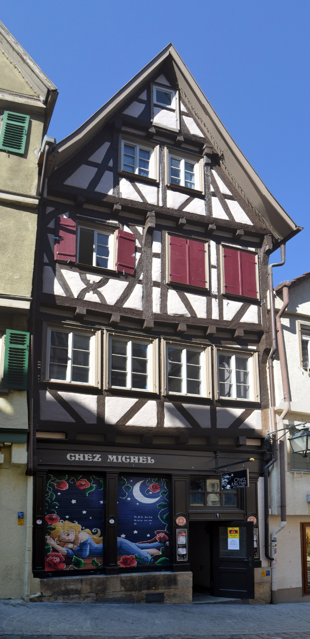 Altes Gebäude mit roten Fensterläden, mehreren Fenstern und einem klaren blauen Himmel im Hintergrund.