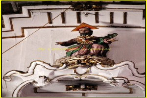 Eine Skulptur und eine Wand mit einem Kabel links und oben sowie einer Birne an der Wand oben.