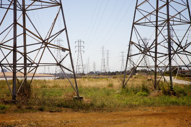 Mehrere Mobilfunkmasten und Kabel vor einem Hintergrund aus Bäumen und Himmel, mit Gras unten.