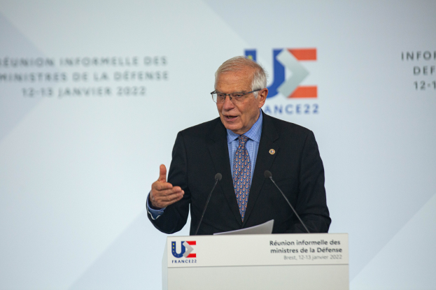 Ein Mann im Anzug und Krawatte hält eine Rede an einem Podium mit zwei Mikrofonen und einem Blatt Papier, vor einem Banner mit der Aufschrift "Ministres de la Défense."
