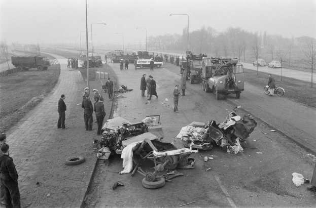 Schwarze und Weiße Szene eines Autounfalls am Straßenrand mit mehreren Fahrzeugen, einer Gruppe von Menschen in der Nähe, Laternenpfählen, Bäumen und dem Himmel im Hintergrund.