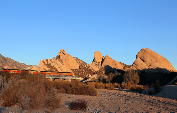 Ein Zug auf einer Brücke mit Felsen und Pflanzen im Hintergrund.