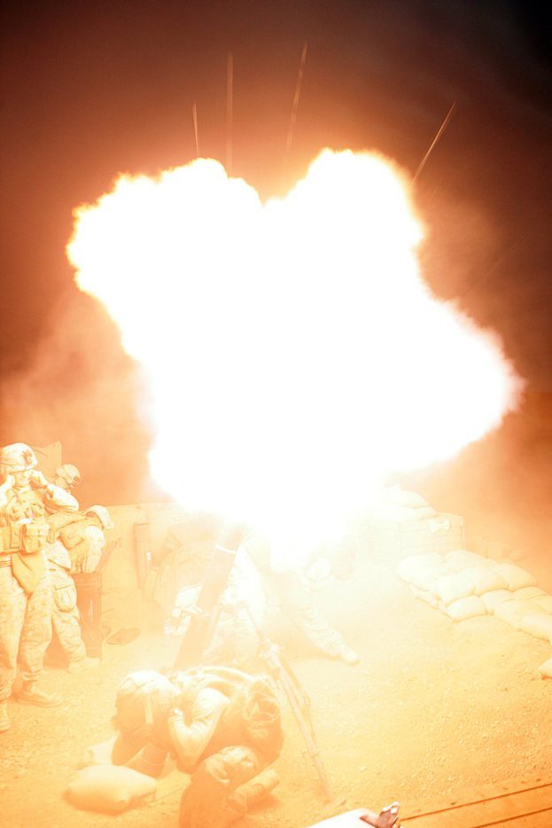 Mehrere Personen in Uniformen und Helmen befinden sich auf einem Gelände mit verstreuten Taschen, mit einem Feuer in der Mitte.