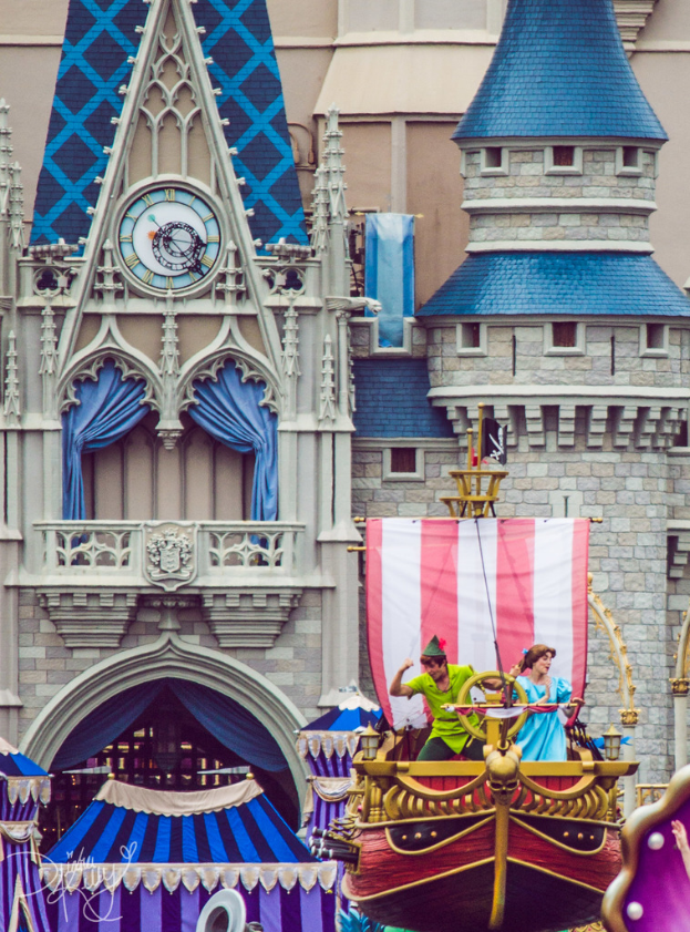 Eine bootähnliche Struktur mit tanzenden Menschen darauf, eine Flagge und ein Gebäude mit einer Uhr und Vorhängen im Hintergrund.