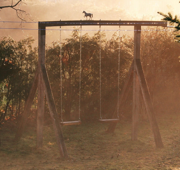 Ein Puppenpferd auf einer Holzschaukel mit einer Gruppe von Bäumen im Hintergrund.