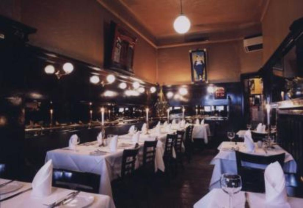 Ein Essbereich mit Gläsern, Kerzenständern, Servietten, Tellern, Stühlen, wandmontierten Rahmen und Deckenleuchten.