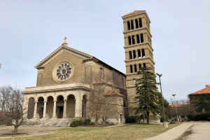 Die Basilika des Heiligen Herzens Jesu in St. Louis, Missouri, eine große Kirche mit einem zentralen Uhrenturm, umgeben von Gebäuden, Straßenlaternen, Fahrzeugen, Bäumen und einem bewölkten Himmel.