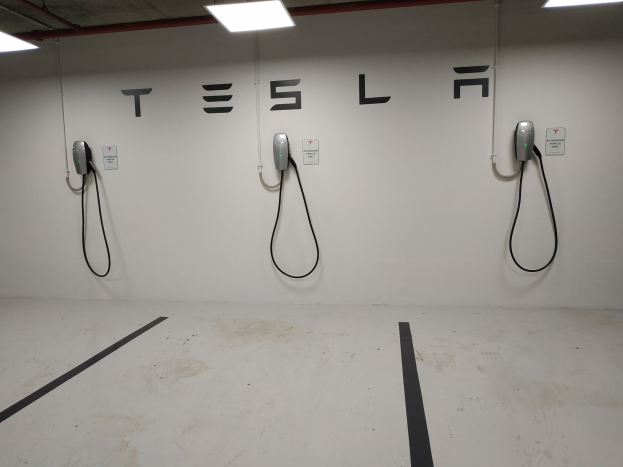 Eine Tesla-Ladestation in einer Tiefgarage mit angebrachten Kabeln und Deckenleuchten, die die darunterliegende Etage zeigen.
