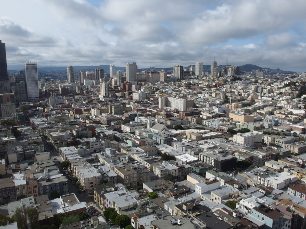 Eine dicht bebaute Stadtlandschaft mit zahlreichen Häusern, Gebäuden und hohen Türmen, mit minimaler Grünfläche und einem Himmel im Hintergrund.