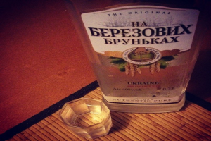 Ein klares Glas mit einer goldenen Flüssigkeit, wahrscheinlich Alkohol, das auf einer dunklen, strukturierten Unterlage steht.