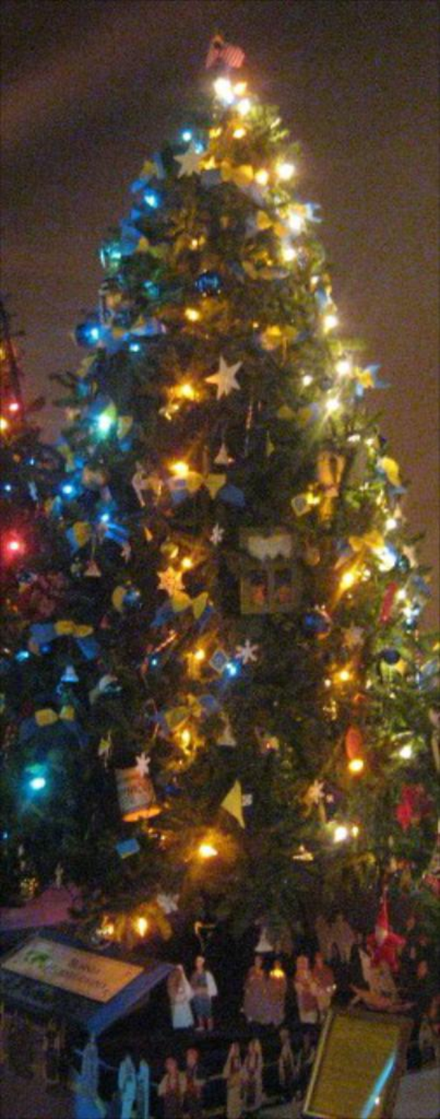 Ein geschmückter Weihnachtsbaum mit Figuren von Menschen auf einem darunterstehenden Tisch.