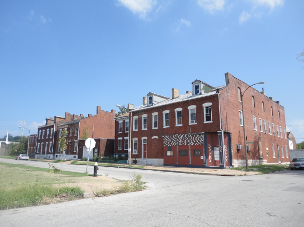 Ein Geb√§ude mit Stra√üenlaternen, Masten und B√§umen, mit Fahrzeugen auf beiden Seiten, einem Gehweg und Gras unten und einem Himmel oben.