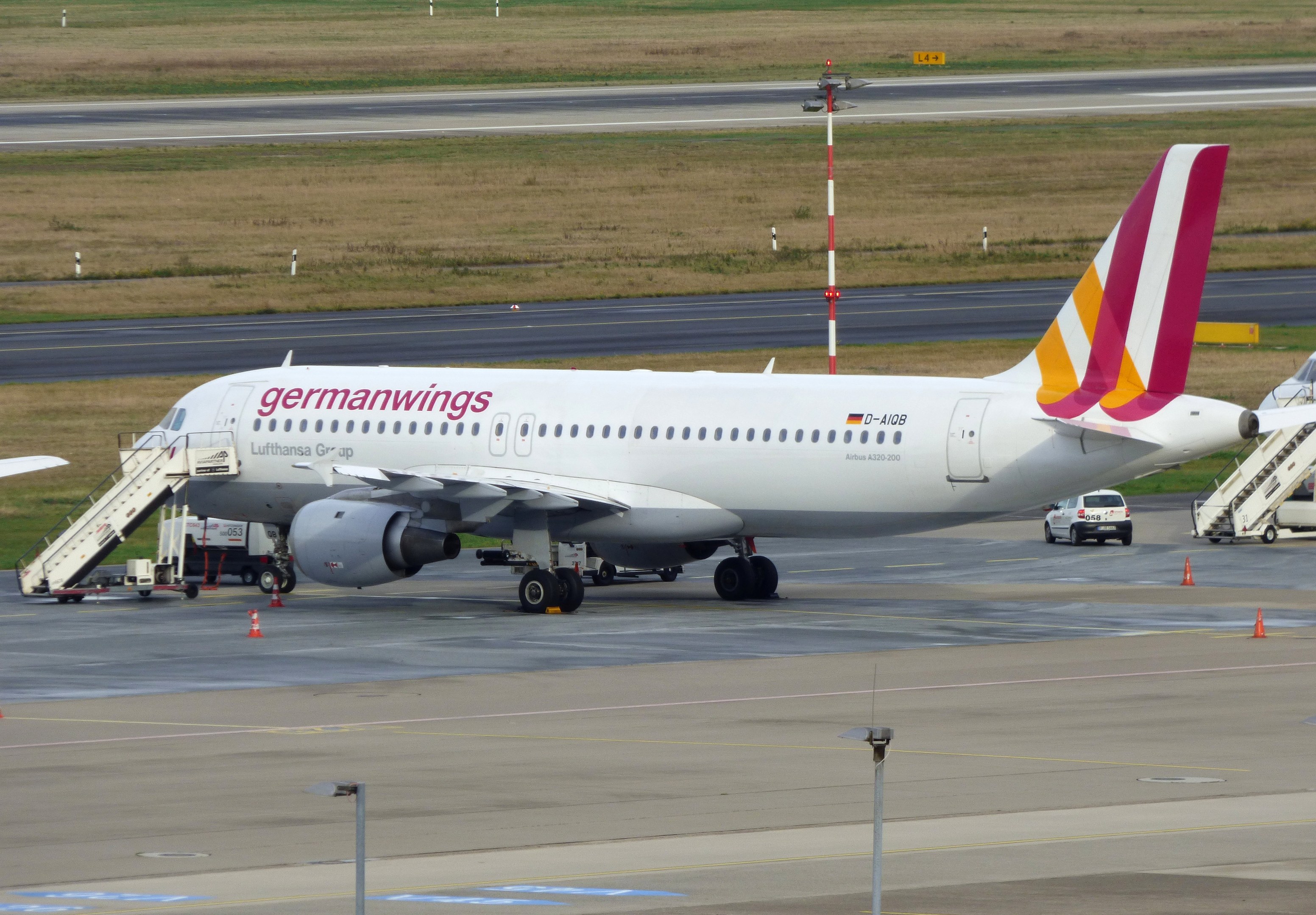 Germanwings Airbus A320-200 auf dem Frankfurter Flughafen geparkt mit Flughafen Servicefahrzeugen, Verkehrskegeln, Versorgungsmasten und Grünfläche im Hintergrund.