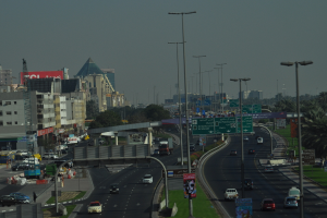 Eine Luftaufnahme einer Stadt mit Gebäuden, Türmen, Kraftfahrzeugen, Werbetafeln, Schildern, Straßen, Bäumen, Straßenlaternen, Menschen, Verkehrskegeln und Informationsanzeigen unter einem klaren Himmel.