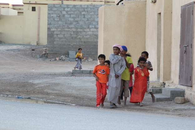Eine Gruppe strahlender Kinder, die "aussern" mit Geb"uden, Wasser, Felsen und einer Stra{\ss}e im Hintergrund.