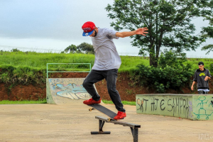 Eine Person fährt in der Mitte des Bildes Schlittschuh, im Hintergrund sind Pflanzen, Bäume, Gras und eine andere Person auf einer Anhöhe zu sehen. Rechts ist eine Wand mit einer Person, ein Weg am Boden und der Himmel oben zu erkennen.