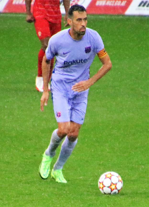 Ein Fussballspieler in Sportkleidung und -schuhen ist im Einsatz auf dem Feld, mit einer Texttafel im Hintergrund.