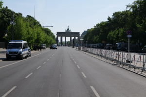 Ein Polizeifahrzeug steht auf der Seite einer vielbefahrenen Straße vor dem Brandenburger Tor in Berlin, Deutschland, mit Barrieren, Schildern, Bäumen, Laternenpfählen und einer bewölkten Himmelovisibilität.