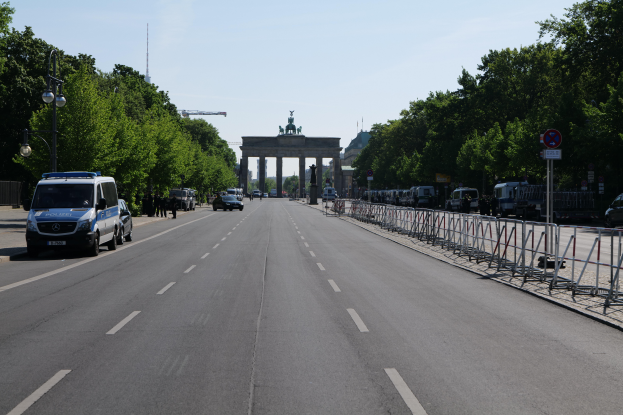 Ein Polizeifahrzeug steht auf der Seite einer vielbefahrenen Straße vor dem Brandenburger Tor in Berlin, Deutschland, mit Barrieren, Schildern, Bäumen, Laternenpfählen und einer bewölkten Himmelovisibilität.