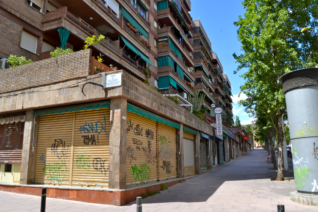 Ein Blick auf Gebäude mit Fenstern, grüne Kleidungsstücke, Geschäfte, Schilder und umgebende Bäume und Pflanzen.