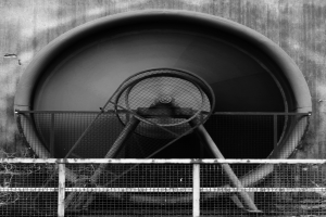 Ein Schwarz-Weiß-Foto eines Abluftgebläses in der Mitte eines Tunnels, umgeben von einem Zaun, mit der Tunnelwand im Hintergrund.