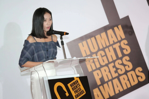 Eine Frau in einem schwarzen Kleid steht an einem Podium mit einem Mikrofon und hält eine Rede bei den Human Rights Press Awards, mit einem konzentrierten und ernsten Gesichtsausdruck.