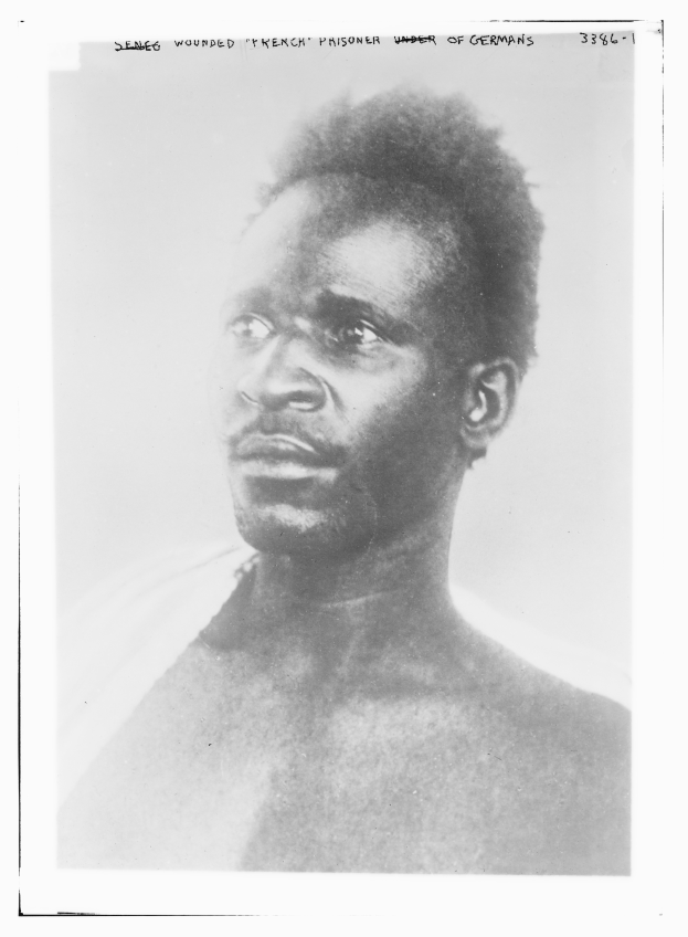 Ein Schwarz-Weiß-Foto eines Mannes mit ernstem Gesichtsausdruck, mit dem Text 'Seneg Verletzter französischer Gefangener unter deutscher Herrschaft' oben.