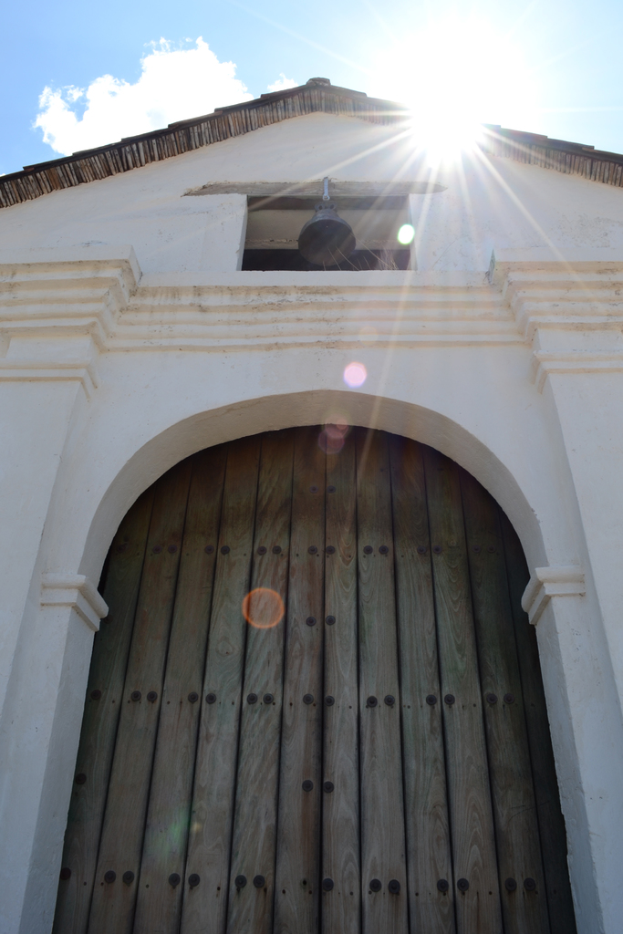 Eine Pfarrgebäude mit einer hölzernen Tür, einer Glocke und einem Dach unter einem klaren Himmel.