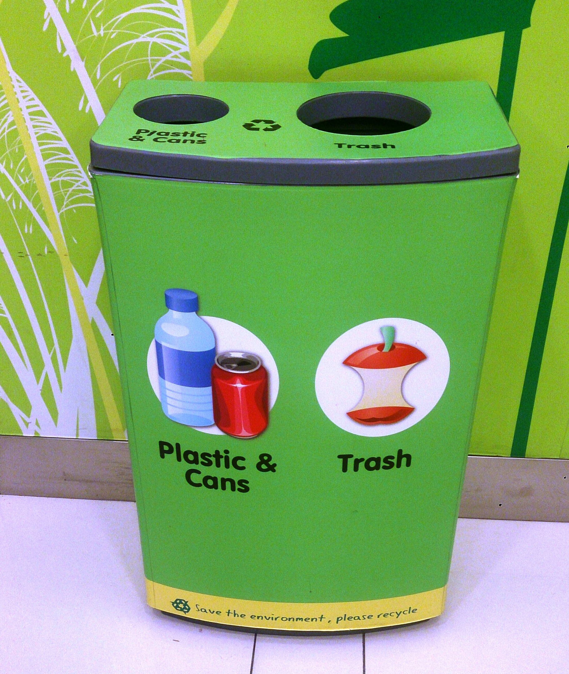 Ein grüner Mülltonne aus Plastik und Dosen auf einem weißen Boden, mit einem Plakat an der Wand im Hintergrund.