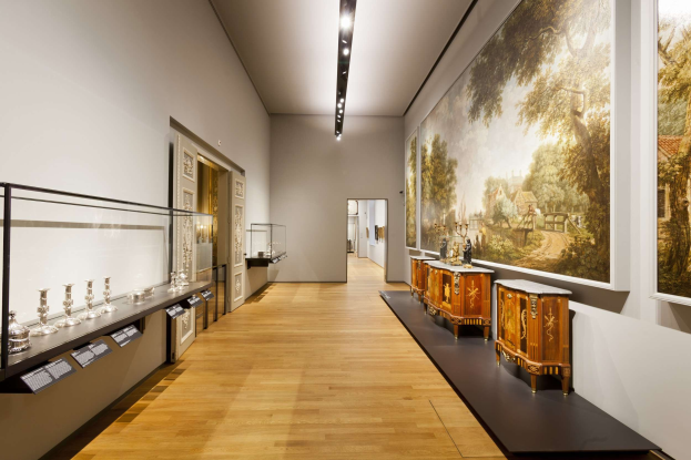 Ein Galerie-Raum im Stedelijk Museum Amsterdam, der verschiedene Kunstwerke wie Gemälde, Skulpturen, eine Glasvitrine, Informationsschilder, Türen und Deckenbeleuchtung zeigt.
