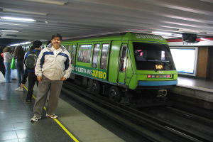 Ein Zug auf Schienen mit Menschen zu seiner Linken und einem Dach an der Spitze des Bildes.