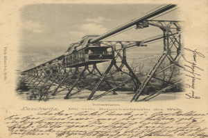 Ein altes Schwarz-Weiß-Foto einer Eisenbahnbrücke mit einem Kran darauf, umgeben von Bäumen und einem bewölkten Himmel, mit dem Text "Bahnstrecka, die erste Eisenbahnbrücke in Deutschland" unten.